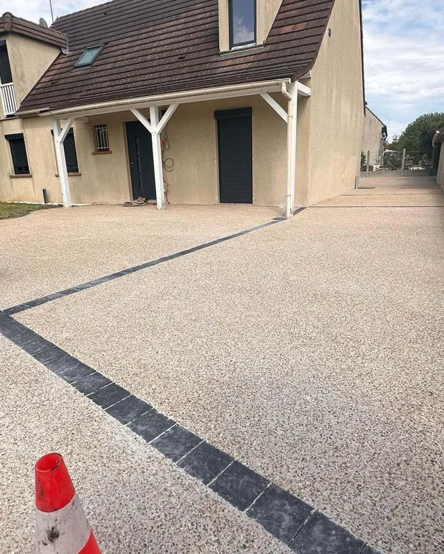 Cour en béton désactivé avec liseré de pavés sombres, le long d'une maison.