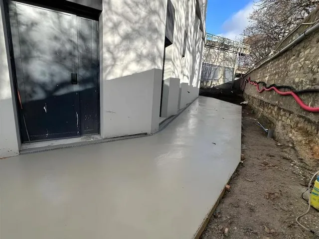 Dalle béton lissée en pied de façade, le long d'un bâtiment.