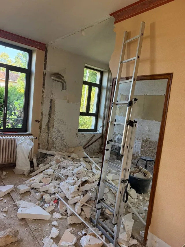 Dépose en cours : enduits retirés jusqu'au mur nu, gravats au sol, échelle en place.