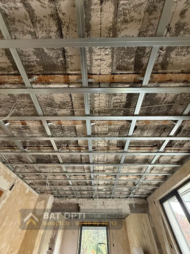 Ossature métallique d'un faux plafond posée sous le plancher, gaines électriques en attente.