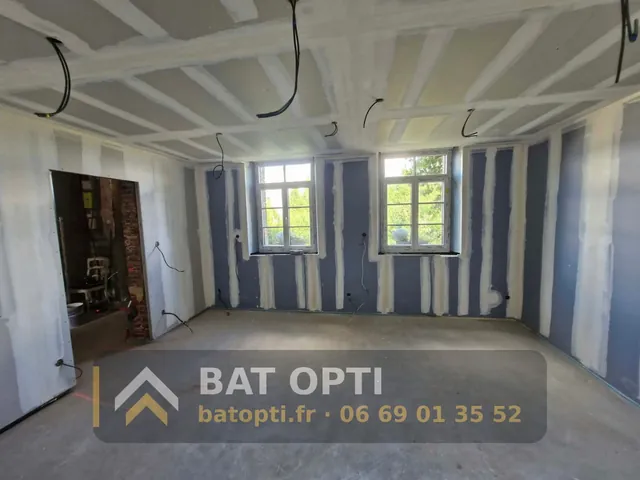 Grande pièce doublée en plaques de plâtre, plafond en plaques, gaines électriques en attente avant finitions.