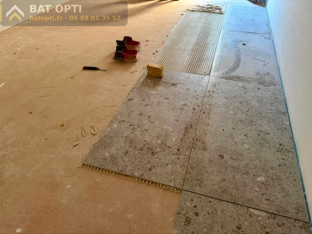 Pose au sol de carreaux grand format effet pierre, rang par rang, avec cales de nivellement.