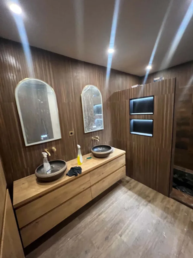 Salle de bain terminée : double vasque sur plan bois, faïence effet bois toute hauteur, faux plafond avec spots et niches rétroéclairées.